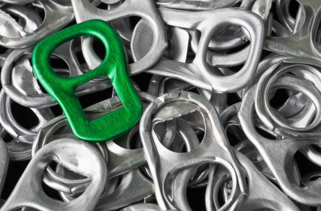 A collection of silver soda can tabs with one being green, symbolizing the impact metal recycling can have on the conversation of energy