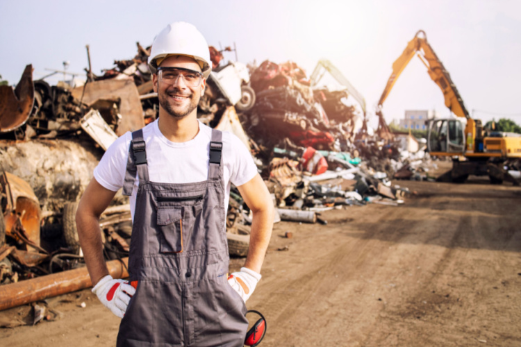 A man working in a scrap metal yard with overalls and a white hard hat